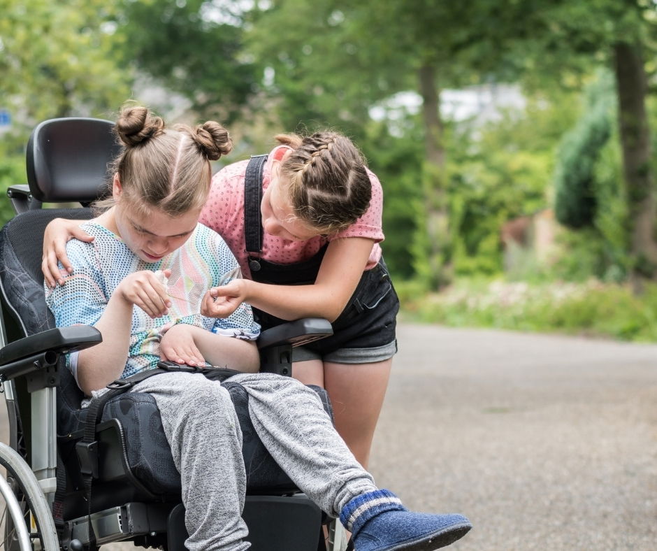 young girl with her arm around disabled girl in wheelchair